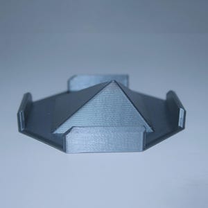 May include: A gray, geometric phone stand with a pyramid-shaped top and rectangular supports. The stand is made of a textured material and has a modern design.