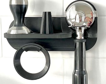 May include: A black espresso machine accessory organiser with a tamper, portafilter, and dosing ring. The organiser is mounted on a white tiled wall. The tamper has a silver base and top. The portafilter is chrome and black.