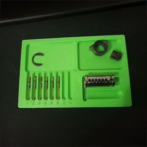 May include: A bright green tray containing locksmithing tools. The tray holds a lock cylinder, pins, a retaining ring, and other small parts. The pins are numbered 1 to 8. The tools are arranged for organisation and easy access.