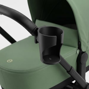 Könnte beinhalten: Ein schwarzer Getränkehalter an einem grünen Kinderwagen befestigt. Der Kinderwagen hat schwarze Details. Der Getränkehalter ist für ein Getränk konzipiert und an der Griffstange des Kinderwagens befestigt.