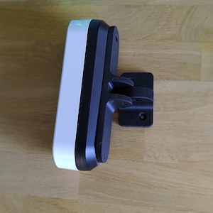 May include: A white and black rectangular device with a black mounting bracket. The device has a curved edge and a smooth, glossy finish. The mounting bracket is attached to the device and has a rectangular base with a curved arm.