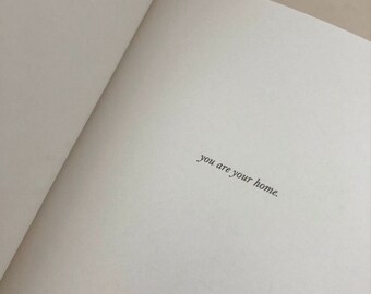 Op de afbeelding: Een open boek met de tekst "you are your home" op een witte pagina.