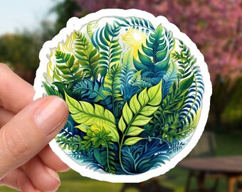 May include: A round sticker with a colorful illustration of a variety of green leaves and ferns. The sticker has a white border and is held in a hand.
