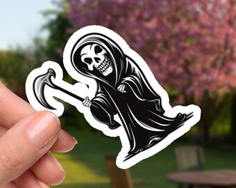May include: A black and white sticker featuring a Grim Reaper character with a scythe. The Grim Reaper is wearing a hooded cloak and has a skull face. The sticker is held in a hand against a blurred outdoor background with trees and a table.