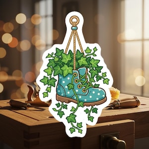 May include: A sticker featuring a cartoon image of a teal boot with white polka dots, filled with green ivy. The boot hangs from a rope, and the ivy spills out and around the boot. The background is blurred.