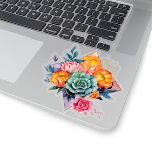 May include: A floral sticker featuring a watercolor design of a bouquet. The bouquet includes orange, yellow, pink, and teal flowers, arranged within a geometric shape. The sticker is placed on a laptop.