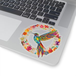 May include: A colorful hummingbird with stained glass-like wings flies through a wreath of flowers. The wreath is made up of red, orange, yellow, green, blue, and purple flowers.