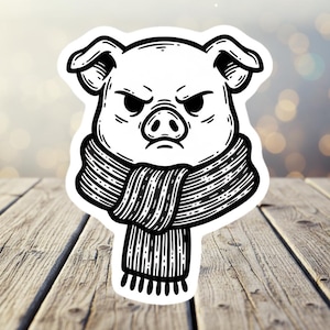 May include: A black and white sticker featuring a cartoon pig with an angry expression. The pig is wearing a striped scarf. The sticker is on a wooden surface.