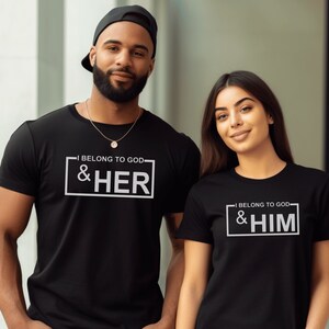 May include: A couple wearing matching black t-shirts with a white graphic print. The man's shirt says "I Belong To God & Her" and the woman's shirt says "I Belong To God & Him".