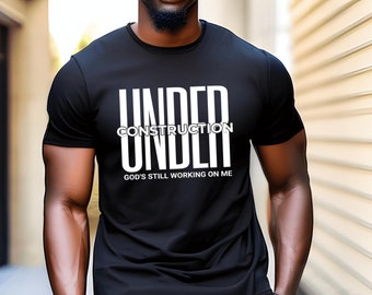 May include: Black t-shirt with white text that reads "UNDER CONSTRUCTION UNDER GOD'S STILL WORKING ON ME".