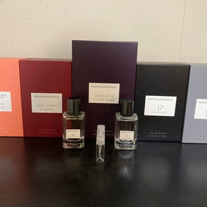 May include: A set of six perfume bottles with different scents from Banana Republic. The bottles are arranged in a row on a dark surface. The scents are: Tuberose Overdose, Dark Cherry & Amber, Tobacco & Tonka Bean, 17 Oud Mosaic, Metal Rain.