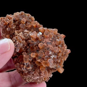 May include: A cluster of aragonite crystals, showcasing a warm, earthy palette of brown and orange hues. The crystals have a hexagonal shape and are clustered together, creating a textured, natural appearance. The background is black.