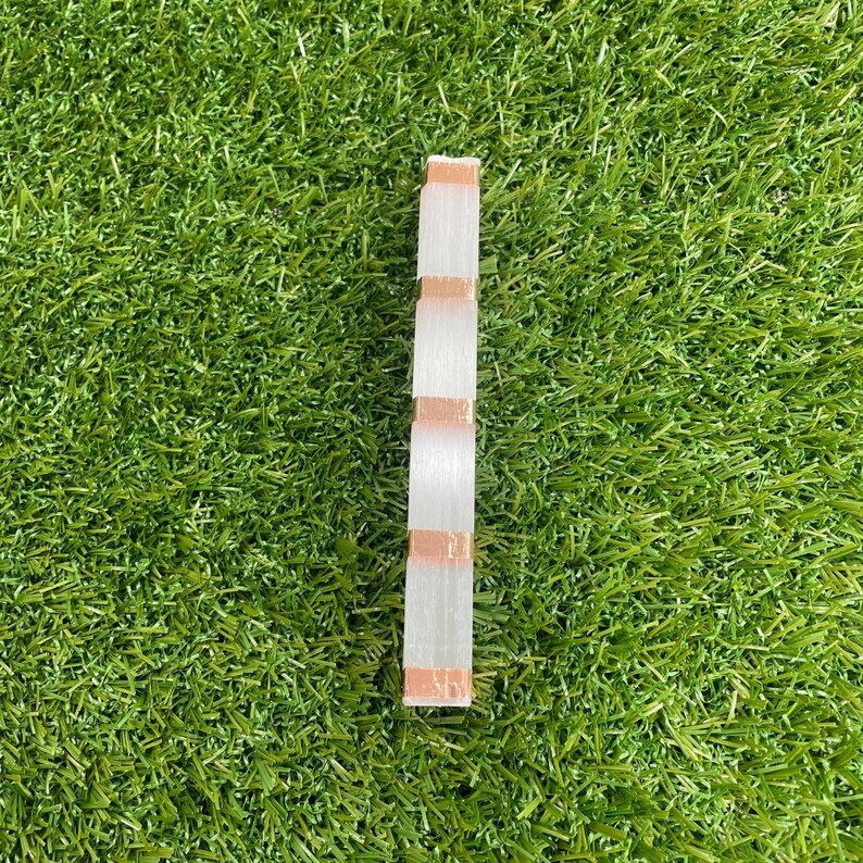 May include: A white and copper striped decorative piece, resembling a stack of blocks, against a green grassy background.