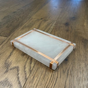 May include: A white rectangular tray with a copper trim around the edges. The tray is made of a smooth, polished material and has a subtle sheen.