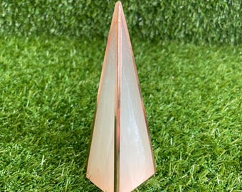 May include: A pyramid-shaped object featuring translucent white panels with a subtle marbled texture, framed by thin, polished copper-colored metal edges that meet at a sharp point at the top, creating a geometric structure with a smooth finish.