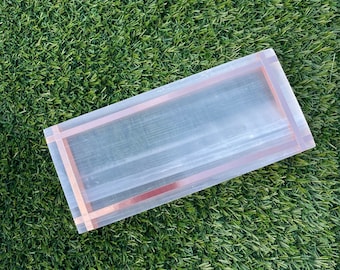 May include: A clear rectangular tray with a rose gold border. The tray is made of a translucent material and has a subtle shimmer.
