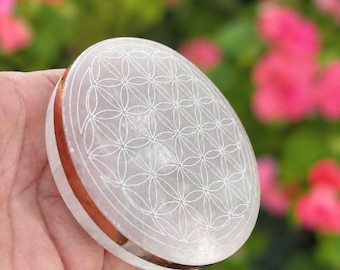 May include: A circular, translucent white stone disc featuring a laser-engraved flower of life geometric pattern on its top surface, accented by a thin, polished copper-colored metallic band encircling the outer edge of the stone object.