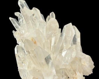 May include: A cluster of clear quartz crystals with sharp, pointed terminations. The crystals are translucent with a slight yellowish hue, and they are arranged in a dense, irregular formation against a black background.