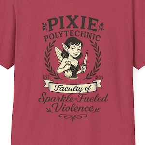 May include: A maroon t-shirt featuring a graphic with the text "PIXIE POLYTECHNIC" above an illustration of a fairy holding a knife. The text "Faculty of Sparkle-Fueled Violence" is below the illustration. The shirt has short sleeves and a crew neck.