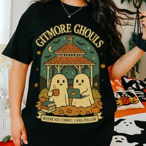 May include: Black t-shirt with a Halloween-themed graphic. The design features two cartoon ghosts under a gazebo, with the words "Gitmore Ghouls" and "Where you commit, I will follow". The shirt is paired with black shorts.
