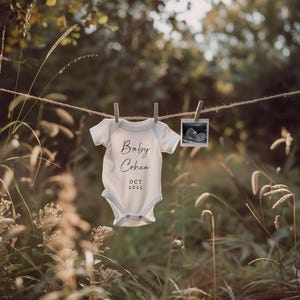 May include: A white baby onesie with the text "Baby Cohen OCT 2025" hanging on a clothesline with a sonogram photo hanging next to it.
