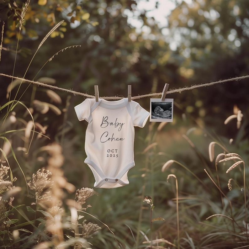 May include: A white baby onesie with the text "Baby Cohen OCT 2025" hanging on a clothesline with a sonogram photo hanging next to it.