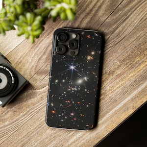 May include: A black phone case with a galaxy print. The case has a camera lens cutout with three black circles.