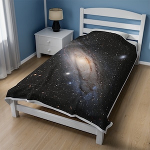 Pu&ograve; includere: Un letto singolo bianco con un copriletto a stampa galassia in bianco e nero. Il copriletto presenta una grande galassia a spirale con un centro giallo brillante.