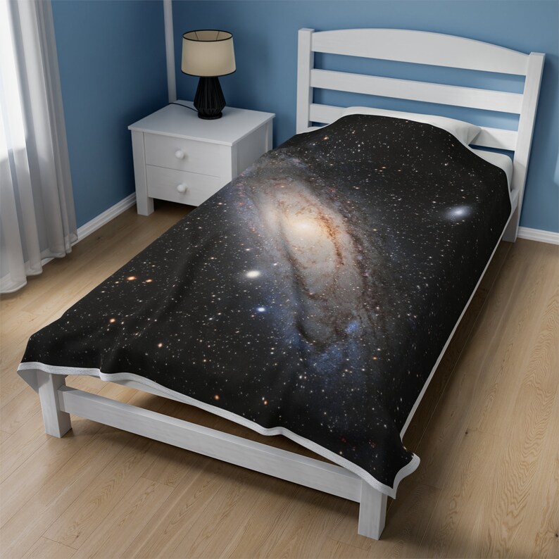 Pu&ograve; includere: Un letto singolo bianco con un copriletto a stampa galassia in bianco e nero. Il copriletto presenta una grande galassia a spirale con un centro giallo brillante.
