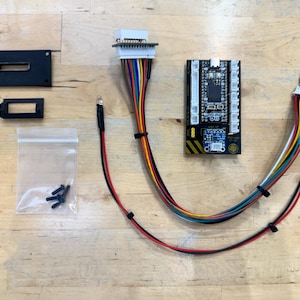Könnte beinhalten: Ein Satz elektronischer Komponenten für ein DIY-Projekt. Das Set enthält eine Platine mit verschiedenen Steckverbindern, eine kleine schwarze Box, eine weiße Box mit Drähten und eine Tüte Schrauben.