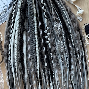 May include: A set of black, white and grey synthetic dreadlocks. The dreadlocks are arranged in a fan shape and are ready to be added to hair.
