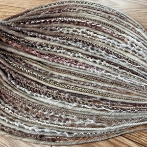 May include: A collection of brown, beige and white synthetic dreadlocks. The dreadlocks are made of different textures and styles, including straight, wavy and curly.