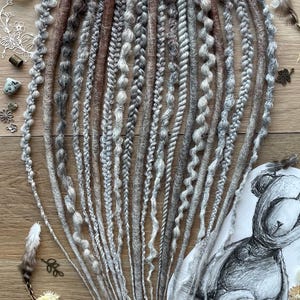 May include: A set of 20 synthetic dreadlocks in shades of grey, brown, and white. The dreadlocks are made with a variety of textures, including smooth, curly, and textured.