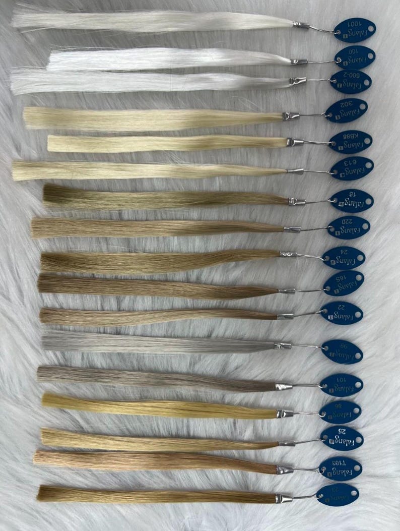 May include: A collection of hair color swatches, each with a different shade of blonde, brown, and gray. Each swatch is attached to a blue tag with the brand name "Falang" and a color code. The swatches are arranged on a white, textured surface.