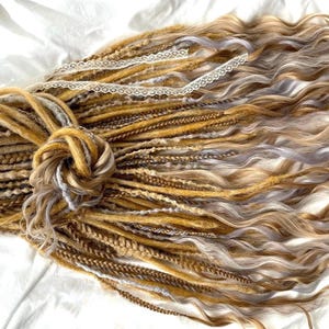 May include: A set of synthetic dreadlocks in shades of blonde, light brown, and gray. The dreadlocks are tied together with a white lace ribbon.