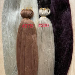 May include: An assortment of synthetic braiding hair extensions in various colors. The colors include silver, white, black, brown, and deep purple. Each bundle is labeled with a number. The hair is bundled at the top with a rubber band.
