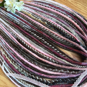 Op de afbeelding: Een bundel synthetische dreadlocks in tinten bruin, roze en wit. De dreadlocks zijn in een cirkelvormige opstelling gerangschikt en zijn bij elkaar gebonden met een wit kantlint.