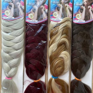 May include: Four packages of Top Remy jumbo braid hair extensions in grey, 118, 27/613, and 6 colours. Each package features a label with a photo of a person with braided hair, the text 100% Kanekalon Fiber, and a colour indicator at the bottom.