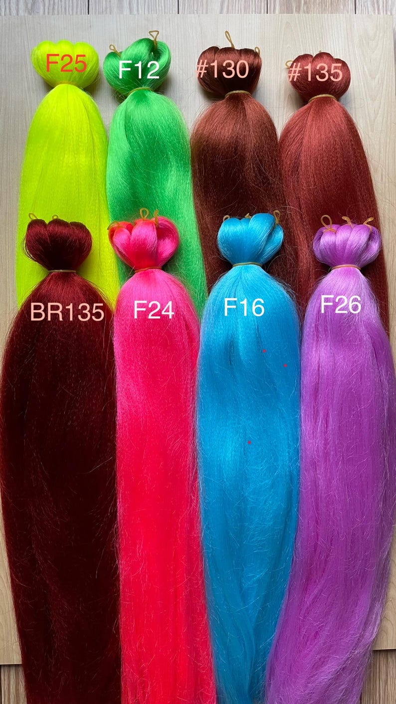 May include: A collection of colorful synthetic braiding hair bundles in various shades, including bright green, pink, blue, and purple. Each bundle is labeled with a code, such as F25, F12, and F24. The hair is arranged vertically, showcasing the vibrant colors.