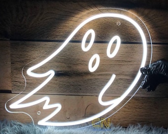 May include: A white neon ghost sign with a smiling face and three oval eyes. The sign is held by a gloved hand against a wooden background. The ghost is outlined in bright white light.
