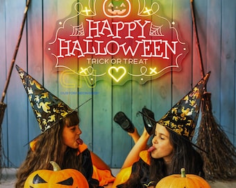 Op de afbeelding: Twee kinderen verkleed als heksen houden gesneden pompoenen vast. Een neonbord met de tekst "Happy Halloween Trick or Treat" hangt aan een muur achter hen.