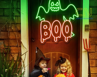 May include: A green neon ghost with a spooky face and the word "BOO" in orange neon. Two children dressed in Halloween costumes are standing in front of the neon sign.