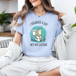 May include: A light blue t-shirt with a frog sitting on a toilet and the text "I tolerate a lot but not lactose".
