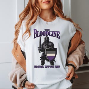Puede incluir: Camiseta blanca con un gr&aacute;fico de un caballero sosteniendo una espada y un escudo. El escudo es negro, blanco y morado. El texto en la camiseta dice "The Bloodline Ends With Me".