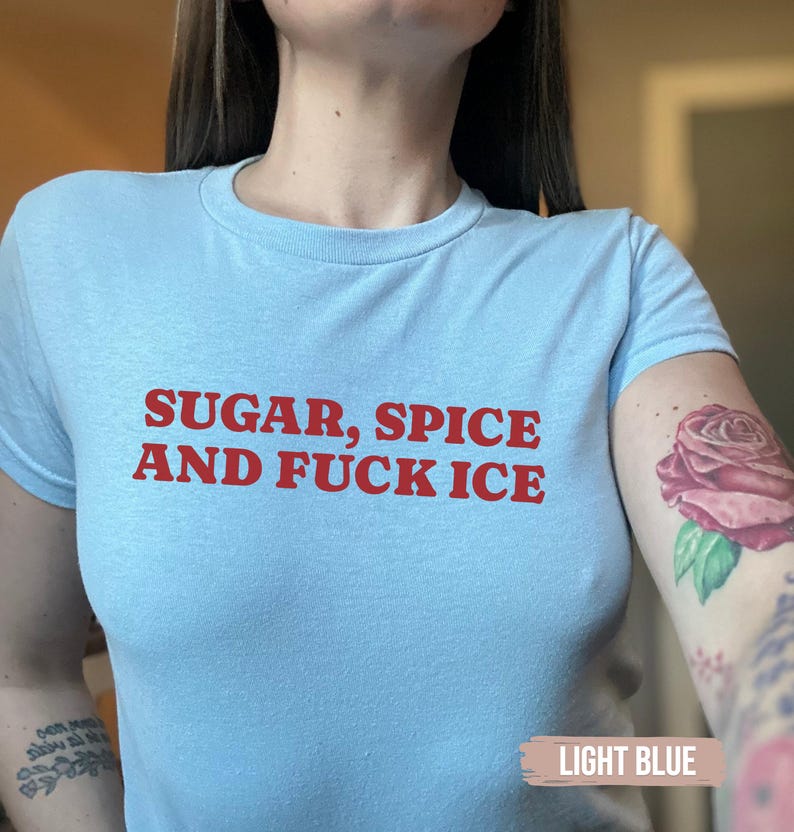 May include: Pale blue crew neck t-shirt with the red text "SUGAR, SPICE AND FUCK ICE". The short-sleeved top is made of a soft fabric. The text is in a bold, sans-serif font.