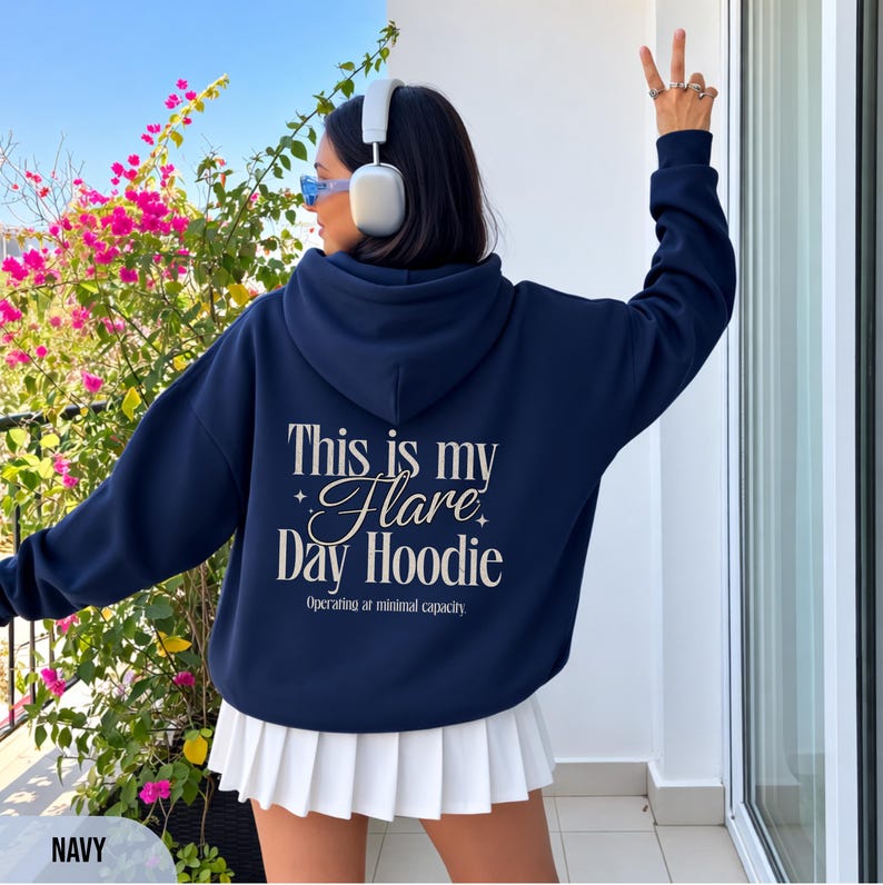 May include: Navy blue hoodie with the text "This is my Flare Day Hoodie" in white script. The hoodie has a drawstring hood and long sleeves. The model is wearing a white pleated skirt and white headphones.