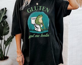 May include: Black heather t-shirt with a graphic of a frog sitting on a toilet and the text "Gluten got me tootin'."