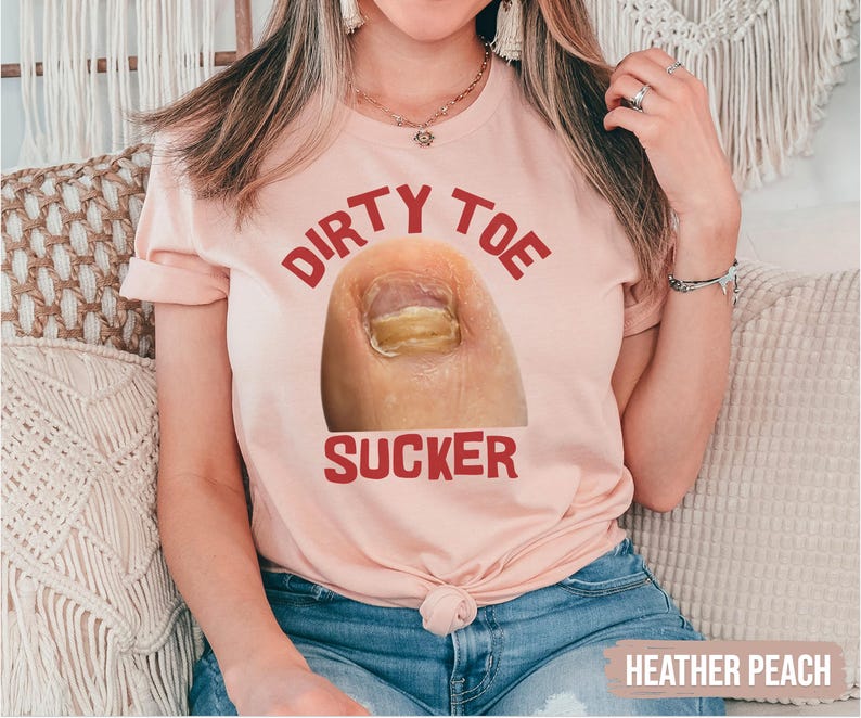 Pu&ograve; includere: T-shirt color pesca con la scritta "DIRTY TOE SUCKER" in rosso. La grafica presenta un primo piano di un dito del piede con un'infezione fungina. La maglietta &egrave; realizzata in materiale morbido ed &egrave; adatta per un abbigliamento casual.