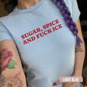 May include: Pale blue t-shirt featuring the red text "SUGAR, SPICE AND FUCK ICE". The t-shirt has a round neck and short sleeves. The fabric appears to be soft and comfortable.