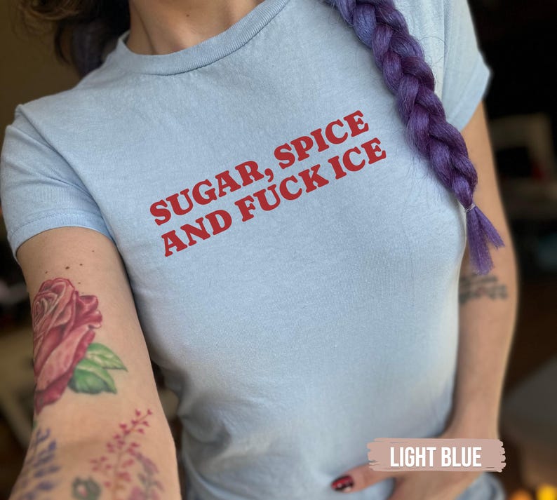 May include: Pale blue t-shirt featuring the red text "SUGAR, SPICE AND FUCK ICE". The t-shirt has a round neck and short sleeves. The fabric appears to be soft and comfortable.